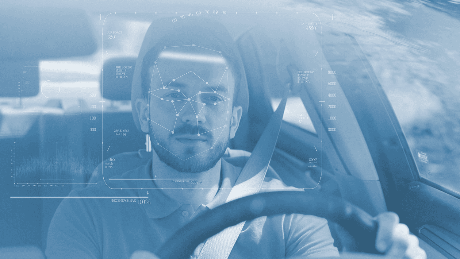 Um motorista dentro de um caminhão, ele está utilizando um boné cinza e uniforme cinza com detalhes amarelos. Está segurando o volante com a mão direita, utilizando cinto de segurança e sorrindo.